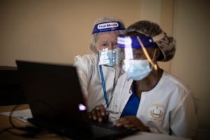 Instructor in mask and face shield oversees student in mask and face shield at computer