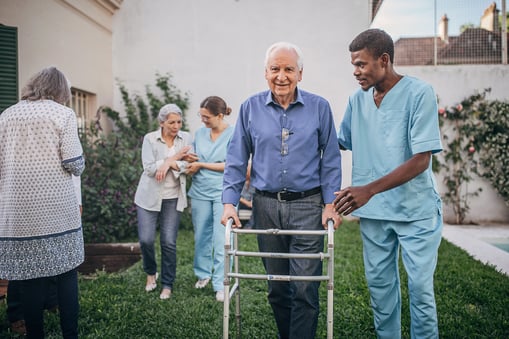 Nurse guiding elderly man with walker