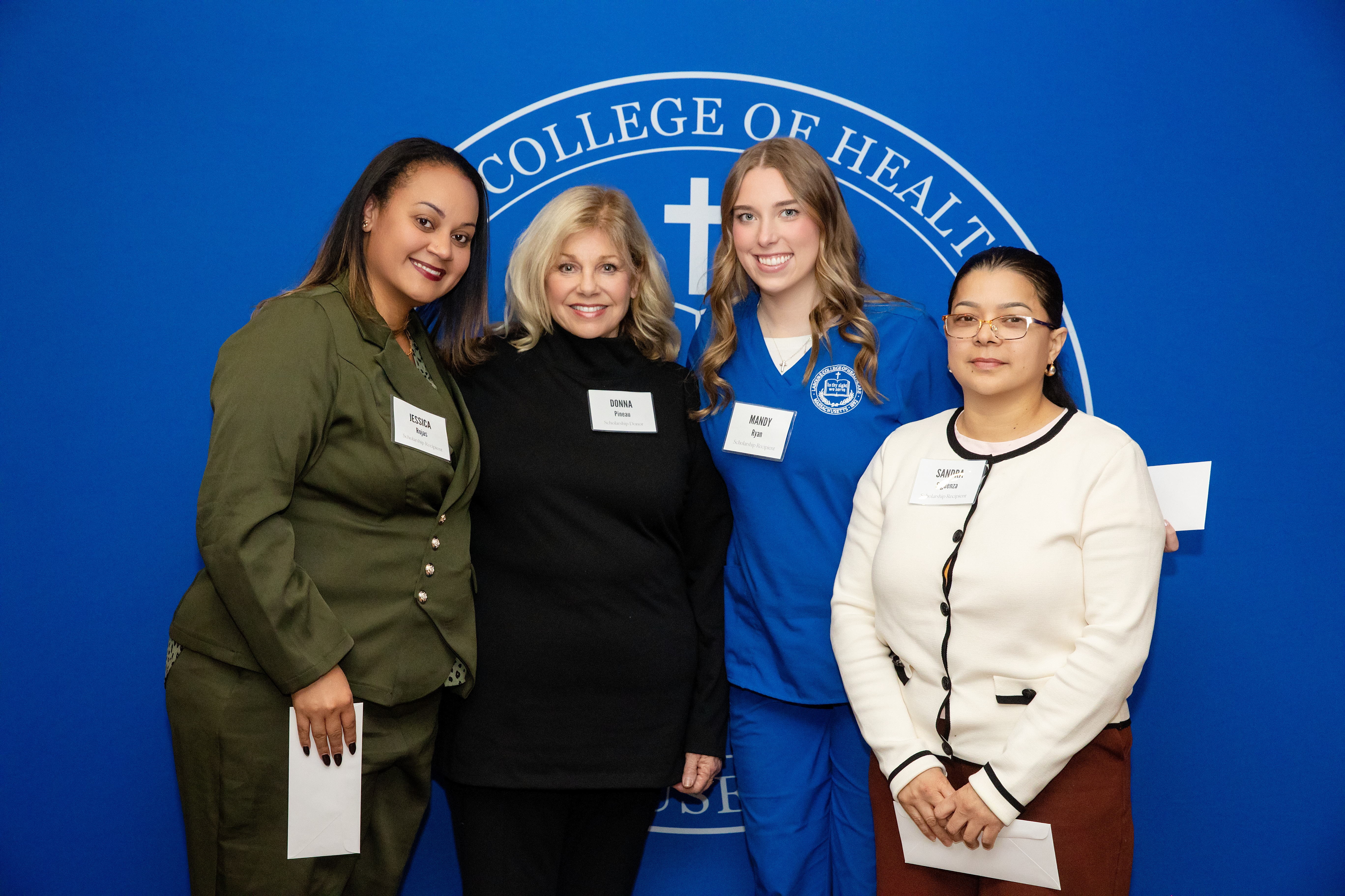 Four women stand in front of a blue screen, three are holding scholarship letters